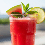 A tall, clear glass of vibrant watermelon juice, garnished with mint and lime, with slight condensation. Alt Text: "Refreshing homemade watermelon juice in a glass with mint and lime garnish